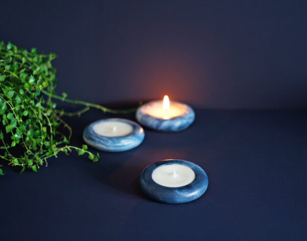 Pequenas velas aromáticas artesanais Élore em suportes azuis marmorizados, dispostas sobre uma superfície escura.