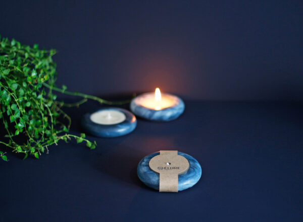 Três velas rosquinhas Élore em tons de azul, uma delas embalada com uma faixa de papel kraft personalizada.