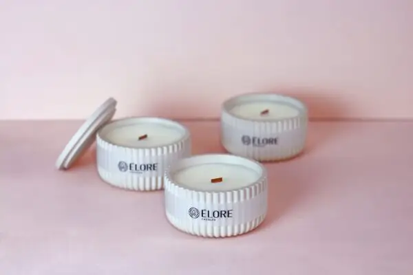 Velas Élore Pureté sobre superfície rosa clara, com foco em três recipientes brancos.