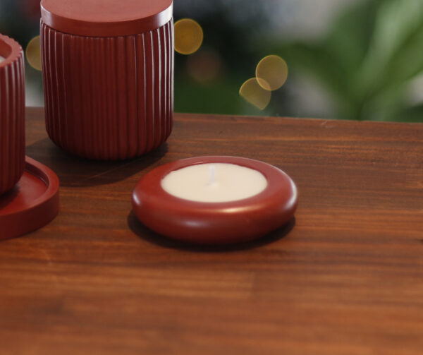 Vela Íris vermelha Élore sobre mesa de madeira, ao lado de velas maiores da mesma coleção.