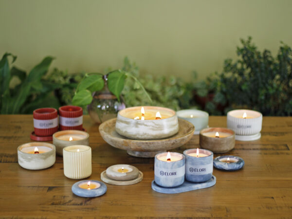 Coleção completa de velas Élore acesas sobre mesa de madeira com plantas ao fundo.
