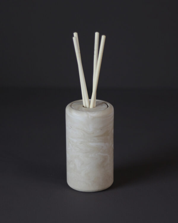 Difusor de varetas Élore em tom marfim marmorizado com fundo escuro e vaso decorativo ao fundo.